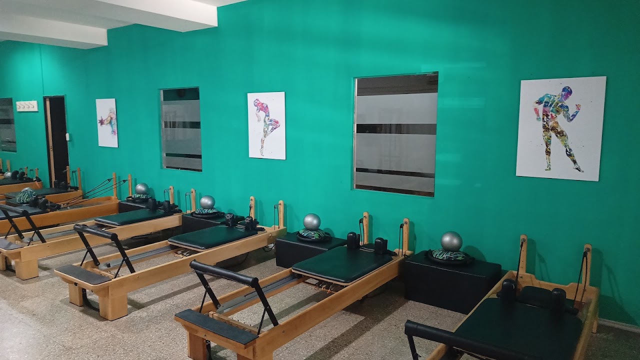 Modern bright pilates reformer studio with teal accent wall and wooden reformer machines with leather carriage pads, warm natural sunlight, clean studio interior